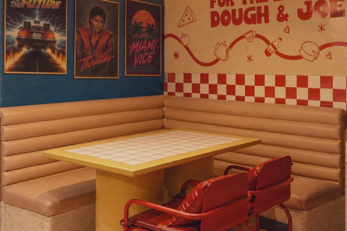 A booth at Dough & Joe on Hill Road, Bandra West, with a tan banquette, red and white check, and eighties film posters on the wall