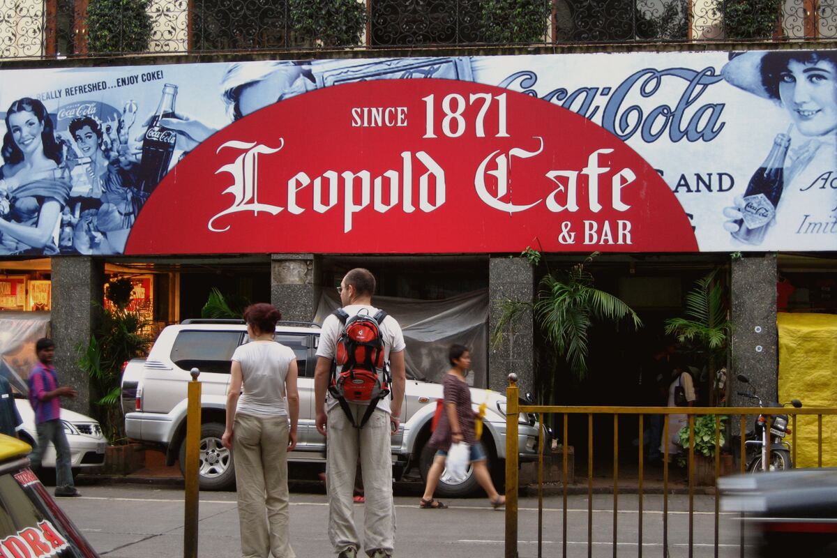 The Leopold Cafe & Bar sign on Colaba Causeway, beneath a wall painted with vintage Coca-Cola advertising