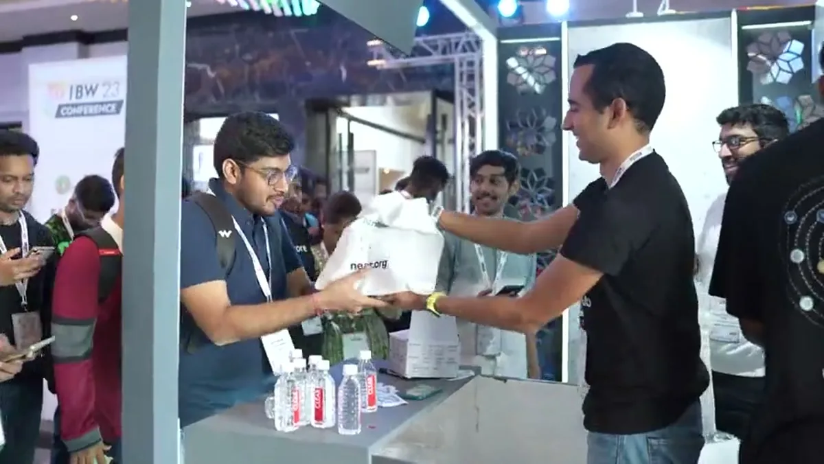 An exhibitor handing a branded item to an attendee at India Blockchain Week 2023